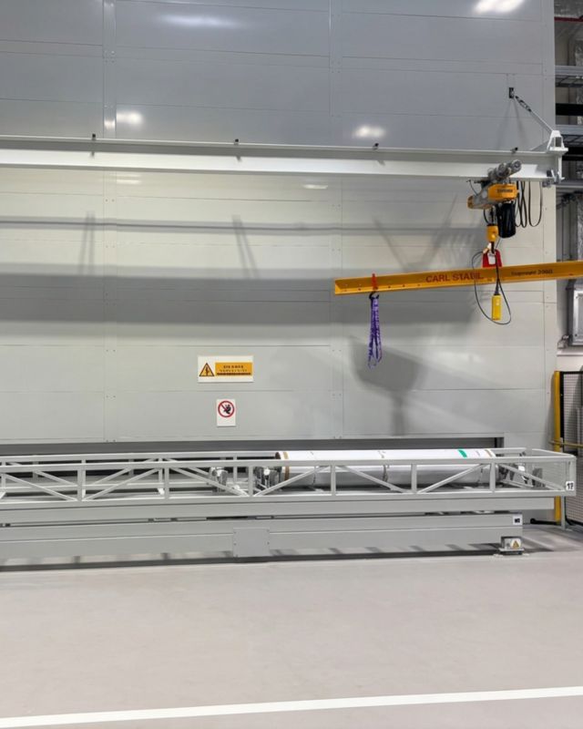 Vollständig eingehauste Long Span Tower Anlage mit integriertem Kransystem für das Be- und Entladen schwerer zylindrischer Materialien in einer Produktionsumgebung.